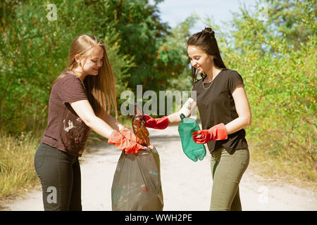 Pulire la nostra casa insieme. Gruppo di volontari riordinano i rifiuti sulla spiaggia nella giornata di sole. Le giovani donne si prendono cura della natura e dell'ambiente, tenendo le bottiglie e i pacchetti via. Concetto di ecologia. Foto Stock