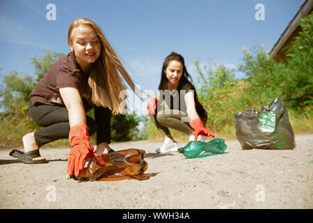 Pulire la nostra casa insieme. Gruppo di volontari riordinano i rifiuti sulla spiaggia nella giornata di sole. Le giovani donne si prendono cura della natura e dell'ambiente, tenendo le bottiglie e i pacchetti via. Concetto di ecologia. Foto Stock