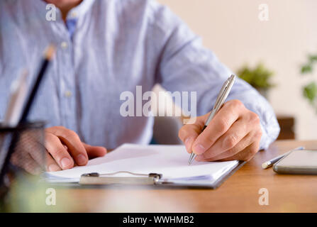 L'uomo iniziando a scrivere sul foglio vuoto su un tavolo di legno vicino. Composizione orizzontale. Vista frontale. Foto Stock