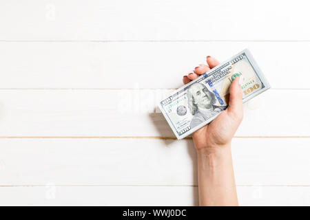 Femmina lato tenendo un fascio di soldi su sfondo colorato. Vista dall'alto di un centinaio di dollari di banconote. Concetto di stipendio con spazio vuoto per il tuo desig Foto Stock