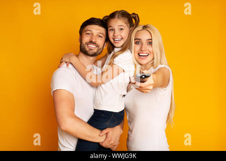 Genitori felici e la figlia di commutazione a guardare i canali TV, Studio Shot Foto Stock