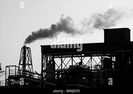 Retroilluminazione industria petrolchimica fumo smog su sky Foto Stock