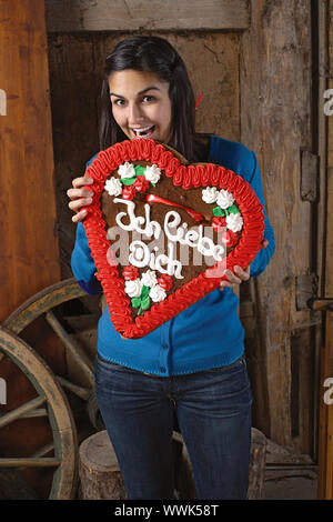 Foto di una bellissima femmina entusiasti di mangiare la sua gigantesca a forma di cuore gingerbread cookie con Ich liebe dich scritto attraverso. Foto Stock