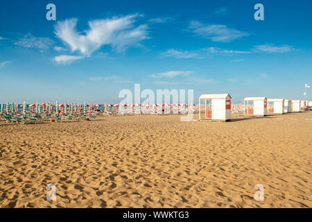 Rossi e bianchi ombrelloni e sunlongers sulla spiaggia sabbiosa Foto Stock