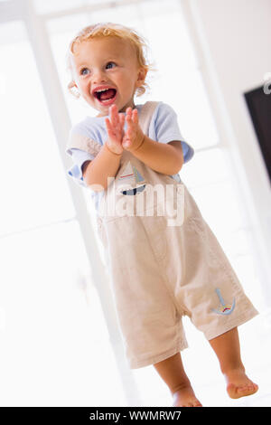 Giovane ragazzo in piedi ad applaudire in interni e sorridente Foto Stock