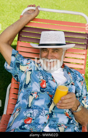 Senior uomo in Prato sedia azienda succo di arancia Foto Stock
