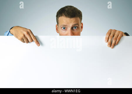 Sorpreso un uomo indica il vuoto bianco poster con lo spazio di copia Foto Stock