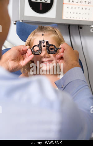 All'ottico optometrista in sala esame con ragazza in sedia a sorridere Foto Stock