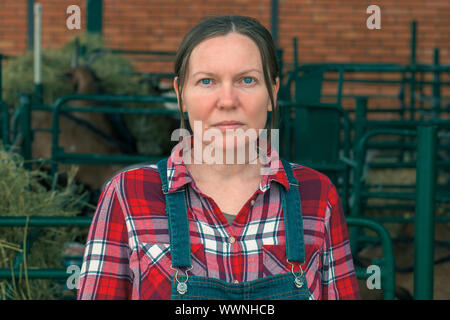 L'agricoltore femmina in posa sull allevamento di capre nella parte anteriore del goatpen Foto Stock
