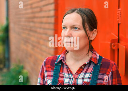 Ritratto di fiducioso agricoltore femmina di fronte al casale guardando la distanza, di pensare e di pianificazione Foto Stock