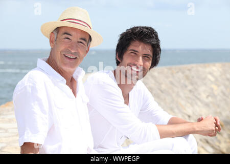 65 anni di vecchio uomo e 30 anni di vecchio uomo seduto sulla sabbia con lo sfondo del mare Foto Stock