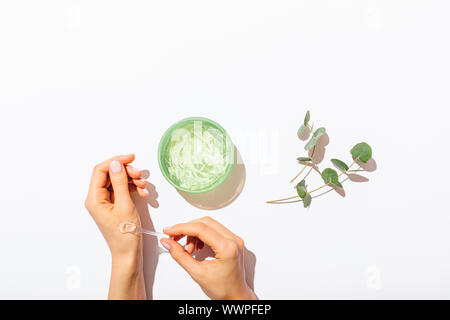 Donna con le mani in mano l'applicazione campione di aloe vera gel accanto a rami di eucalipto su bianco tavola piana cosmetici composizione laici. Foto Stock