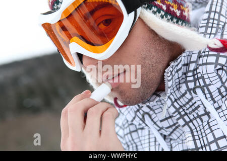 Giovane sciatore mettendo panna fredda lip stick sulle labbra Foto Stock