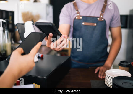 Il cliente effettuando il pagamento utilizzando la tecnologia NFS al caffè cafe. Proprietario di piccola impresa e contactless o wireless concetto di pagamento. Foto Stock