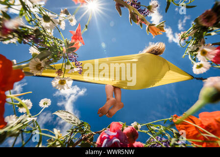 Ragazza rilassante in un amaca circondata da fiori in una giornata di sole Foto Stock