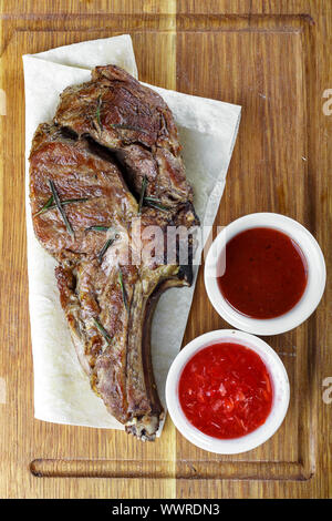 Deliziosa bistecca con l'osso. Bistecca servita su un tagliere di legno con due tipi di salse Foto Stock