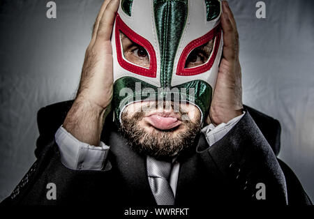 Imprenditore arrabbiato con maschera di lottatore messicano, vestito in tuta e tirante Foto Stock