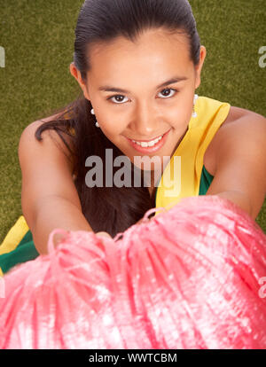 Sorridente Cheerleader con la sua pom pom seduto sull'erba Foto Stock