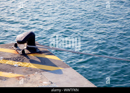 Bollard in porto con la corda avvolta attorno e linee di colore giallo su nero Foto Stock