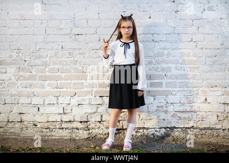 Schoolgirl permanente bianco contro un muro di mattoni dello sfondo. Bambino ragazza in uniforme scolastica in posa. Foto Stock