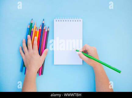 Bambino con le mani in mano azienda matite colorate e un notebook su sfondo blu con copyspace. Piatto stile di laici. Si torna a scuola concetto. Foto Stock