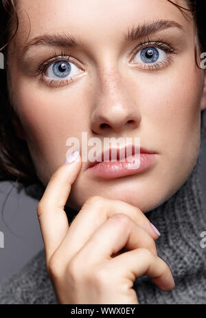 Bellezza Ritratto di giovane donna in grigio maglione di lana. Bruna ragazza con luminosi occhi blu e giorno trucco femminile Foto Stock