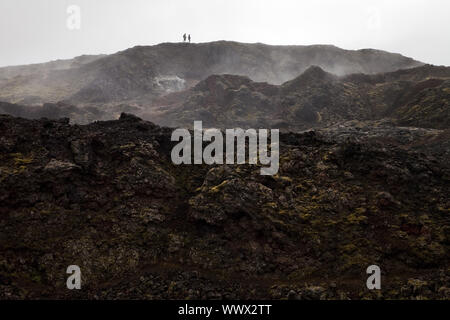 I turisti in rocce laviche del vulcano Krafla, area geotermale Leirhnjukur in background, Islanda, Europa Foto Stock