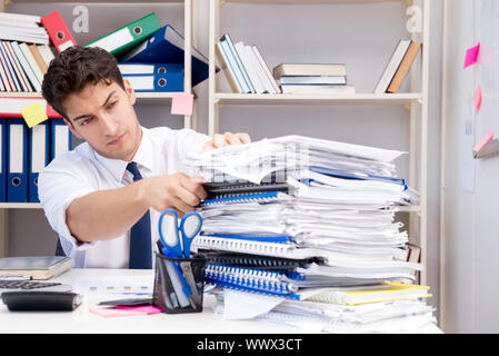 Imprenditore lavora in ufficio con pile di libri e giornali Foto Stock