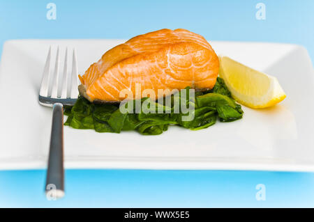 Bistecca di salmone su letto di spinaci e decorate con il limone Foto Stock