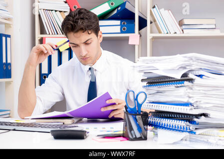 Imprenditore lavora in ufficio con pile di libri e giornali Foto Stock