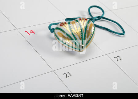 Ceramica a forma di cuore ciondolo giacente sul calendario pagina punti per San Valentino Foto Stock
