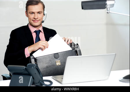 Maschio di call center disponendo esecutivo opere di carta e il loro mantenimento in modo sicuro in borsa Foto Stock