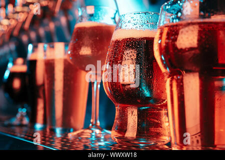 Bicchieri di chiaro e scuro birra, ale, lager, stout, porter in moderne e luminose luci al neon con macchina di colata sullo sfondo. Concetto di vacanza, divertimento, sale riunioni, oktoberfest, grandi amici' party. Foto Stock