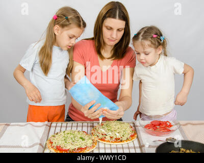 Due bambine sta guardando con interesse come la madre di irrigazione è la maionese pizza Foto Stock