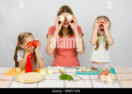 La mamma con due bambine divertirsi al tavolo della cucina a giocare con le verdure Foto Stock