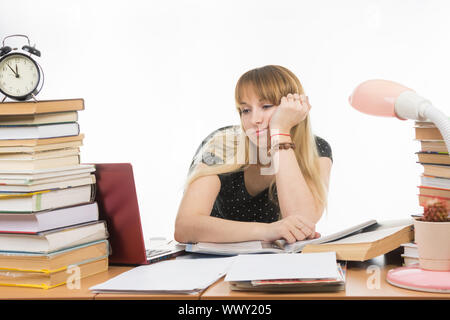 Purtroppo lo studente esamina il computer portatile al tavolo tra le pile di libri e giornali Foto Stock