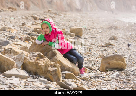 Un annoiato stanco ragazza stabilisce su una grande roccia in riva al mare Foto Stock