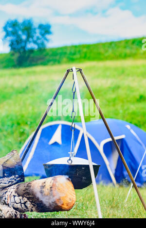 Un camp-steaky fuligginosa food bowl appeso su un treppiede su un fuoco Foto Stock