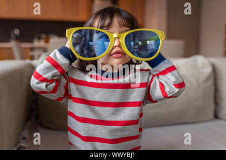 Carino bambina giocando con grandi novità occhiali da sole a casa Foto Stock