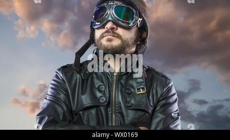 Orgogliosi, pilota del 20s con occhiali da sole e vintage aviatore casco. Indossa giacca di pelle, barba e facce espressive Foto Stock