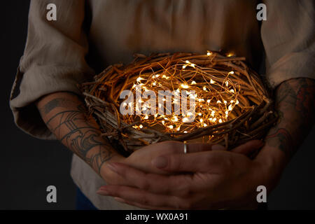 Nido con le luci di Natale nelle mani della donna su sfondo nero Foto Stock