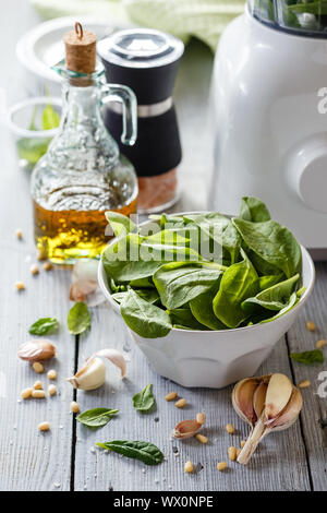 Pesto di spinaci in un vasetto di vetro, decorazione: foglie di spinaci, pinoli, formaggio parmigiano, aglio, olio d'oliva. Foto Stock