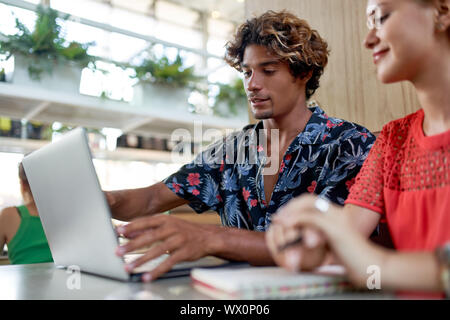 Schietto stile di vita colpo di attraente multi-etnico millenario di pianificazione dei colleghi sul computer allo stand del moderno e luminoso tanga tropicale cafe Foto Stock