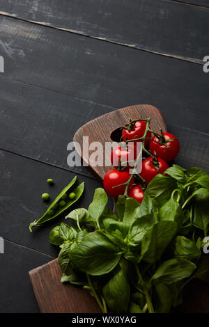 Ortaggi freschi pomodori con basilico e piselli verdi su una tavola di legno Foto Stock