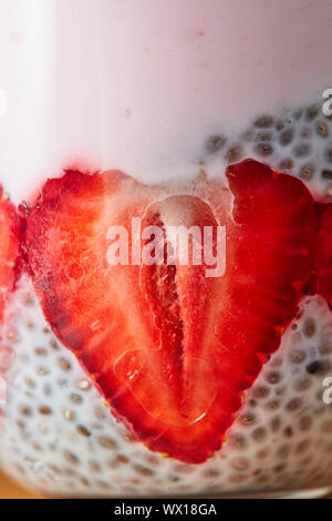 Foto macro di una metà di fragola con semi di Chia e yogurt in un vetro trasparente. Foto Stock