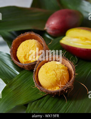 Gelato al mango sorbetti nella buccia di cocco con mezza mango fresco su foglie di palmo Foto Stock