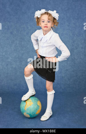 Schoolgirl mettere piede sul globo come un pallone da calcio Foto Stock