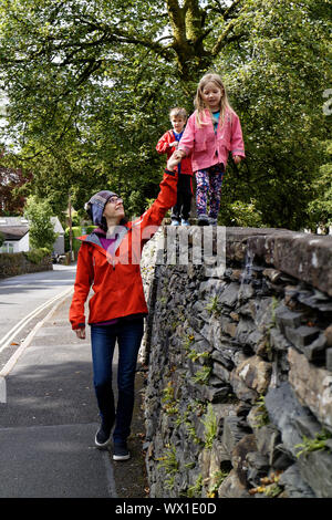 Una mamma tenendo le mani con sua figlia (4 anni) come lei cammina lungo la parte superiore di una parete Foto Stock