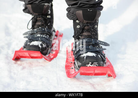 Le racchette da neve. Escursioni con le racchette da neve closeup. Red nuovo moderno high-end di racchette da neve. L'uomo escursioni nella neve sulla neve giorno d'inverno. Foto Stock