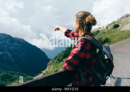 Vista dal retro di una donna punti un dito in montagna Foto Stock
